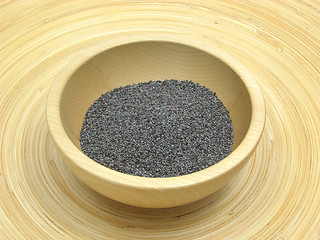 Image showing Wooden bowl with poppy seeds on bamboo plate