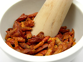 Image showing Pestling dried red hot chili pepper in a bowl of chinaware