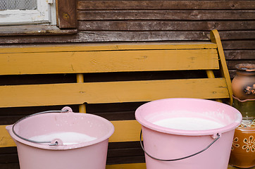 Image showing two pink pail full fresh cow milk on wooden bench 