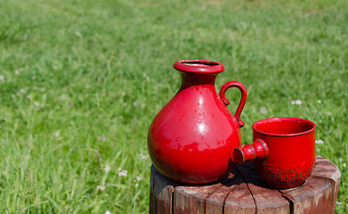 Image showing ceramic red water jug and cup on stump on nature  