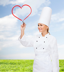 Image showing smiling female chef drawing red heart on air