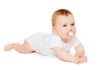 Image showing smiling baby lying on floor with dummy in mouth