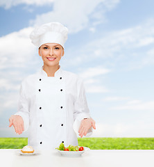 Image showing smiling female chef with salad and cake on plates