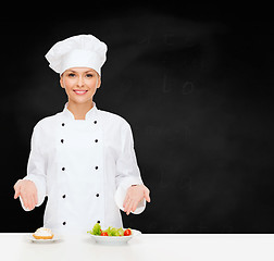 Image showing smiling female chef with salad and cake on plates