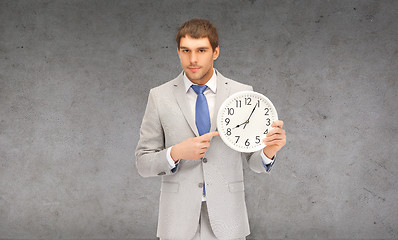Image showing handsome businessman pointing finger to wall clock