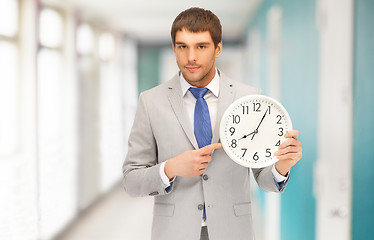 Image showing handsome businessman pointing finger to wall clock