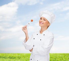 Image showing smiling female chef with fork and tomato