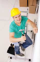 Image showing smiling man in helmet hammering nail in wall