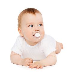 Image showing smiling baby lying on floor with dummy in mouth