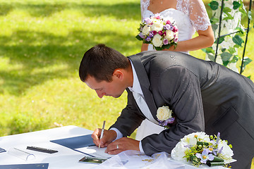 Image showing groom signing certificate in park 