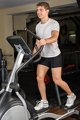 Image showing young man does workout at elliptical trainer in gym