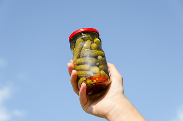 Image showing cucumber jar in female hand on blue sky background 