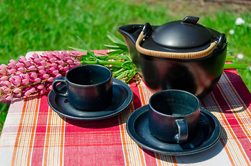 Image showing close up black clay tea set and lupine aoutdoor  
