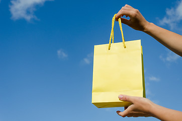 Image showing hand hold yellow paper bag on blue sky background 