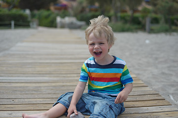 Image showing Flashy boy sits on a wooden walkway on the beach