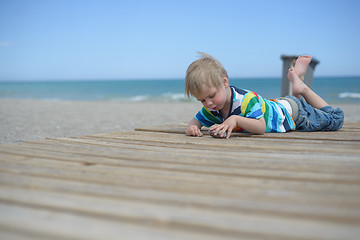 Image showing Boy resting on a wooden walkway on the beach