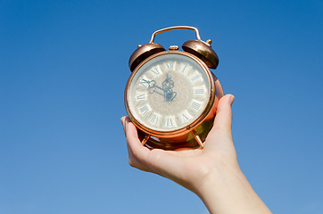 Image showing clock roman numeral in hand on blue sky background 