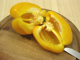 Image showing Halved yellow pepper on wooden plate  with knife