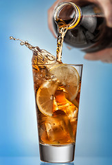 Image showing Glass of splashing iced tea with lemon on blue background