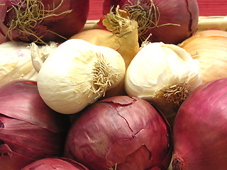 Image showing Onions and garlics in a basket in front of red background