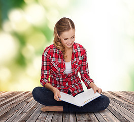 Image showing smiling young woman sitting on floor with book