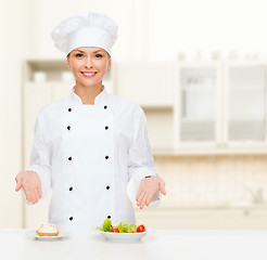 Image showing smiling female chef with salad and cake on plates