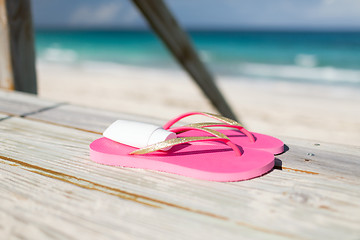 Image showing close up of sunscreen and slippers at seaside