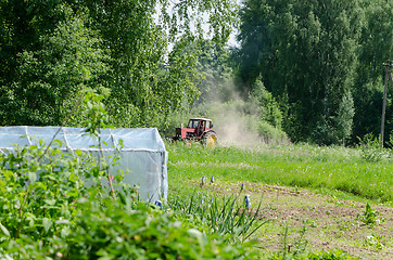 Image showing small red tractor harrow ground  near homestead 