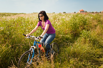 Image showing Woman riding bicycle in meadow