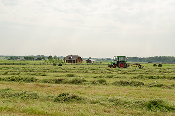 Image showing tractor turning raking cut hay in field 