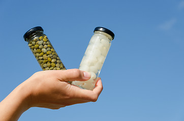 Image showing hand hold caper garlic jar on blue sky background 