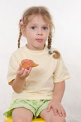 Image showing Girl chews thoughtfully bun sitting on a chair