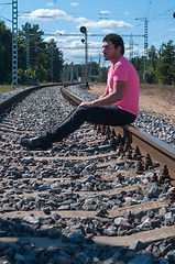 Image showing Single man in pink t-shirt sitting on train tracks