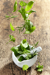 Image showing green herbs falling into mortar and pestle