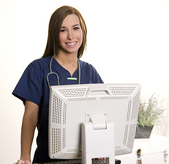 Image showing Working Nurse Smiles Looking over Monitor at Computer Workstatio