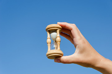 Image showing hand hold wooden hourglass on blue sky background 