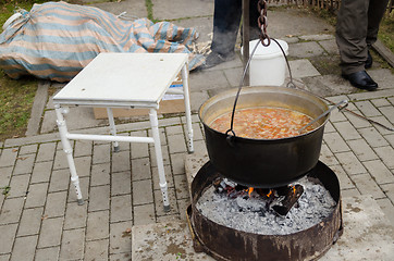 Image showing black pot full of rustic soup on open fire outdoor 