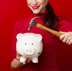 Image showing Smiling Woman in Red Holds Hammer Above Piggy Bank Savings