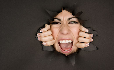 Image showing Pretty Female Face Breaking In Through Black Paper