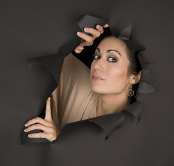 Image showing Beautiful Brunette Woman Looks Sideways Through Torn Hole