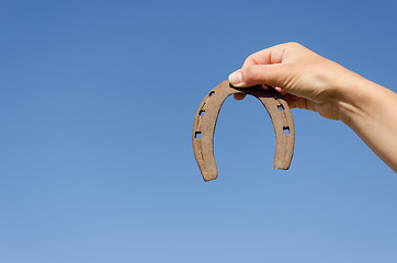 Image showing rusty iron horseshoe in hand on blue sky bckground 