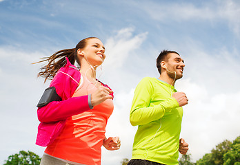 Image showing smiling couple with earphones running outdoors