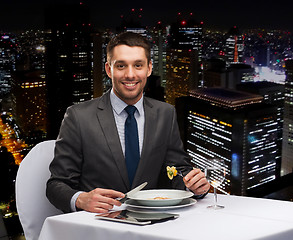 Image showing smiling man with tablet pc eating main course