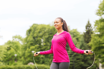 Image showing smiling woman exercising with jump-rope outdoors