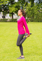 Image showing smiling black woman stretching leg outdoors