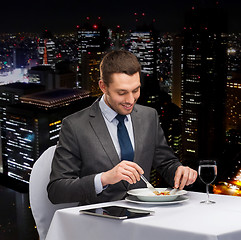 Image showing smiling man with tablet pc eating main course