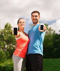 Image showing two smiling people with smartphones outdoors