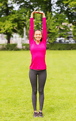 Image showing smiling black woman stretching leg outdoors