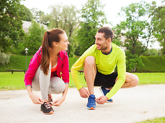 Image showing smiling couple tying shoelaces outdoors