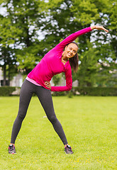 Image showing smiling black woman stretching leg outdoors